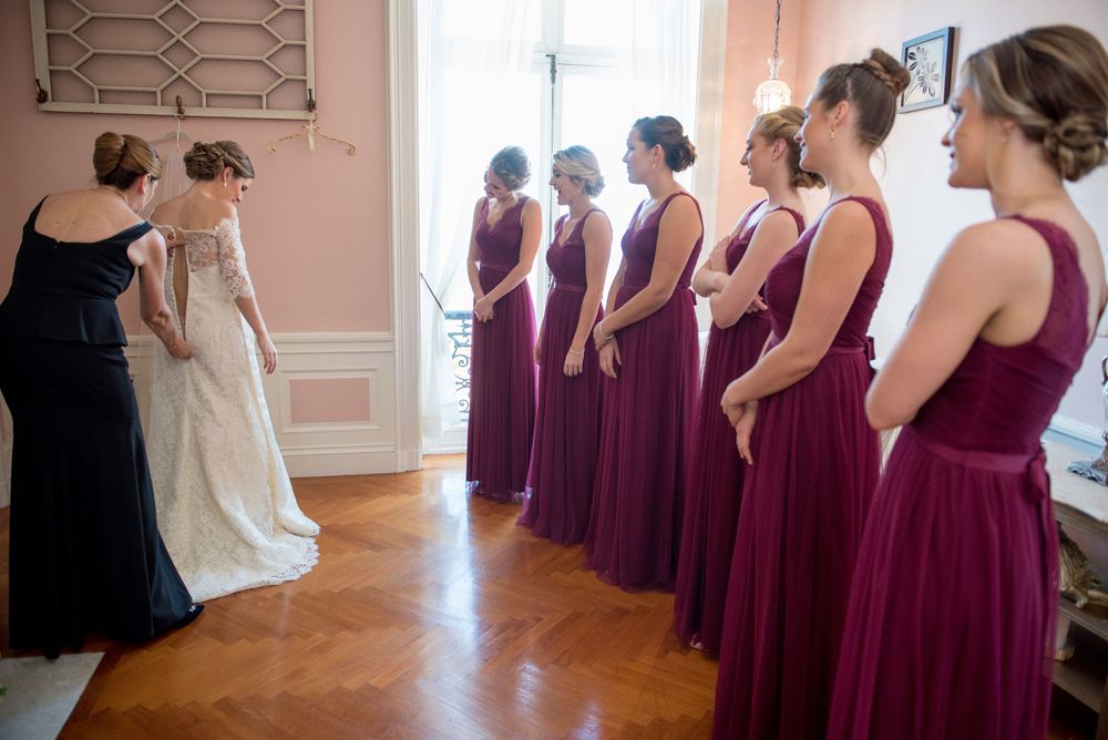 Bridesmaids in deep purple gowns lined up in an elegant room with pink walls.