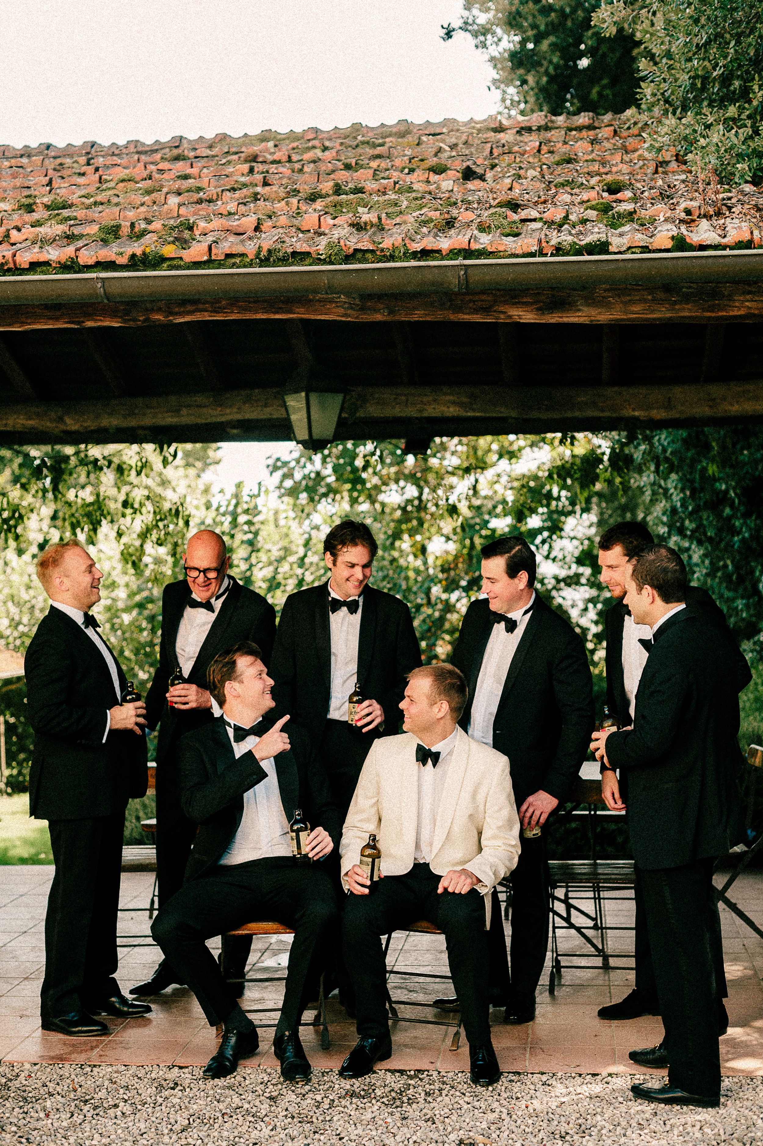 Large group of formally dressed guests socializing under covered outdoor terrace.