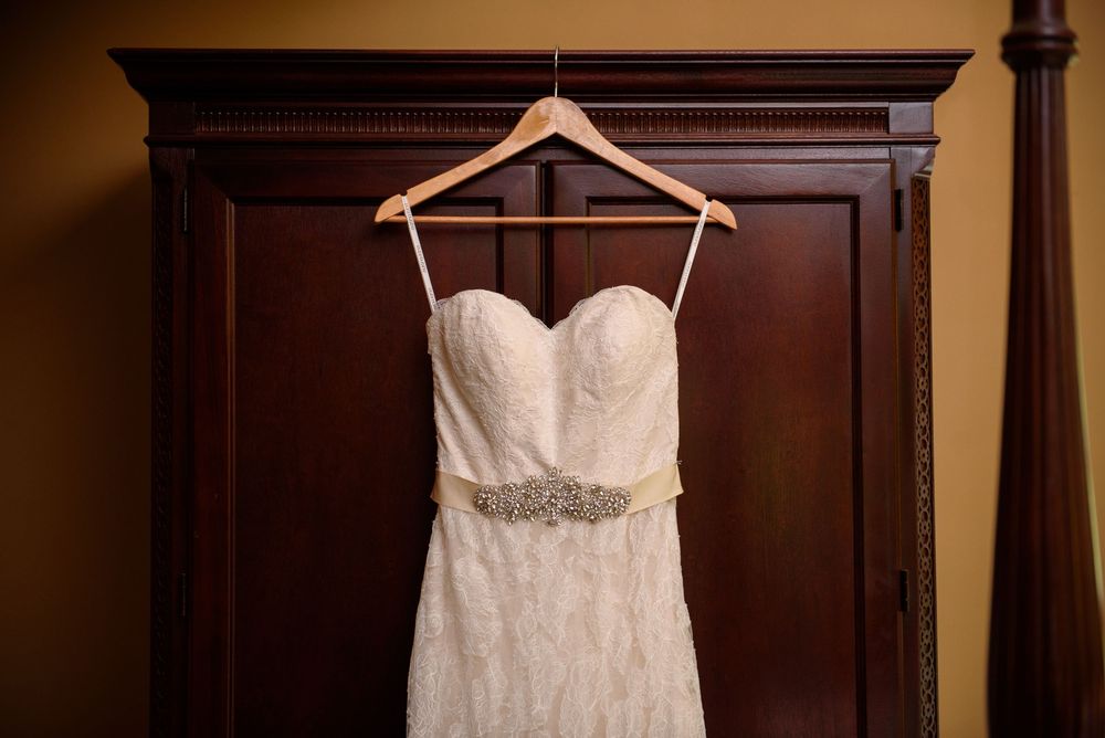 Three elegant white wedding dresses displayed on hangers against a dark wood wall.