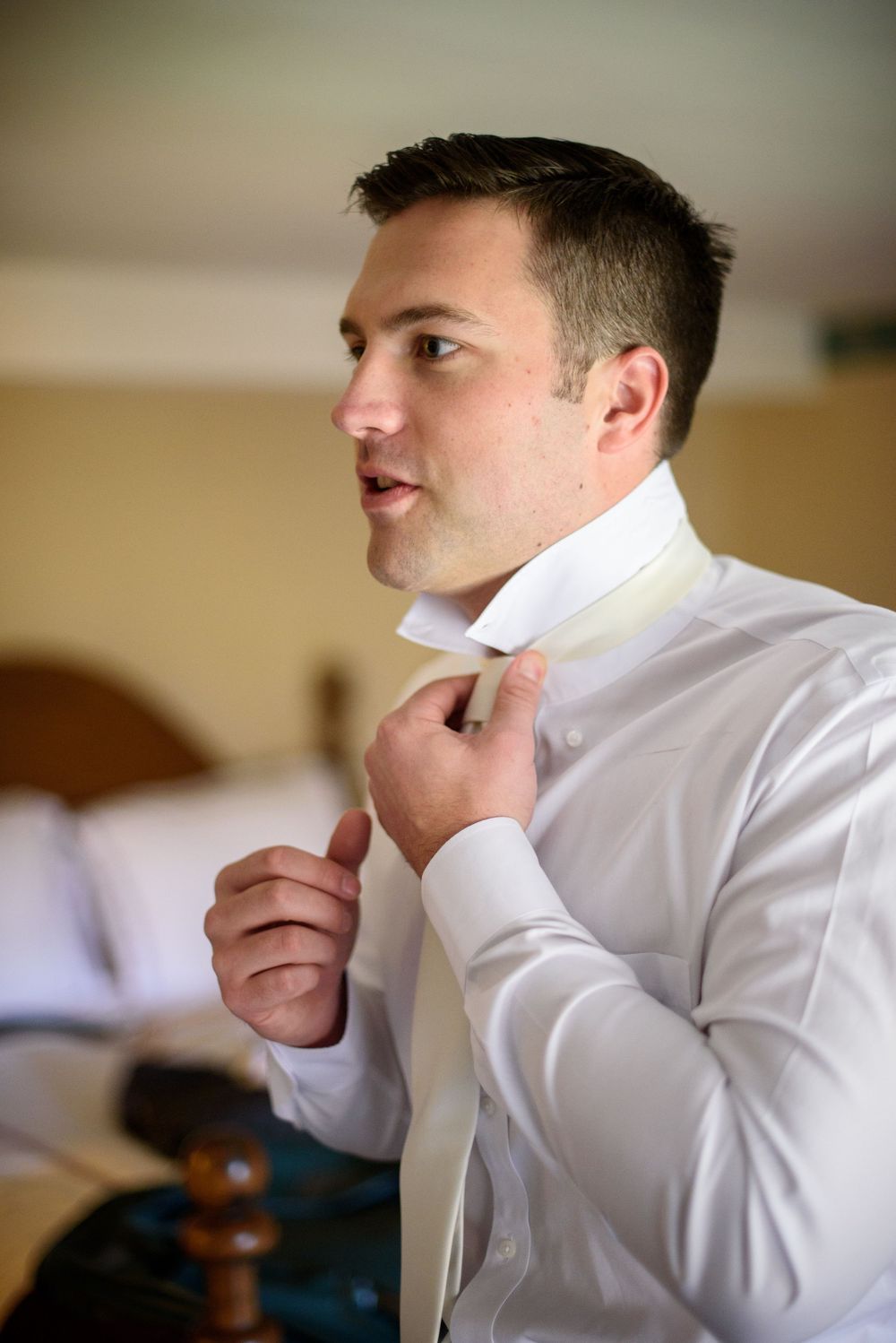 Person in white dress shirt adjusting collar in profile view.