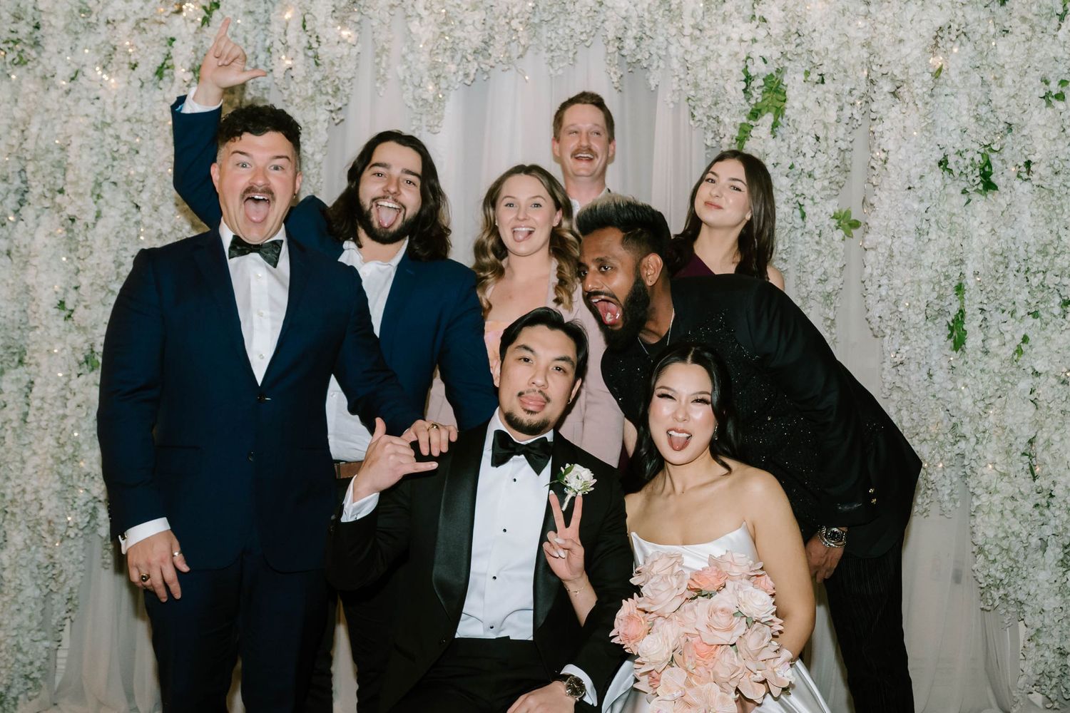 A group in formal attire poses together at an event against a textured white backdrop.