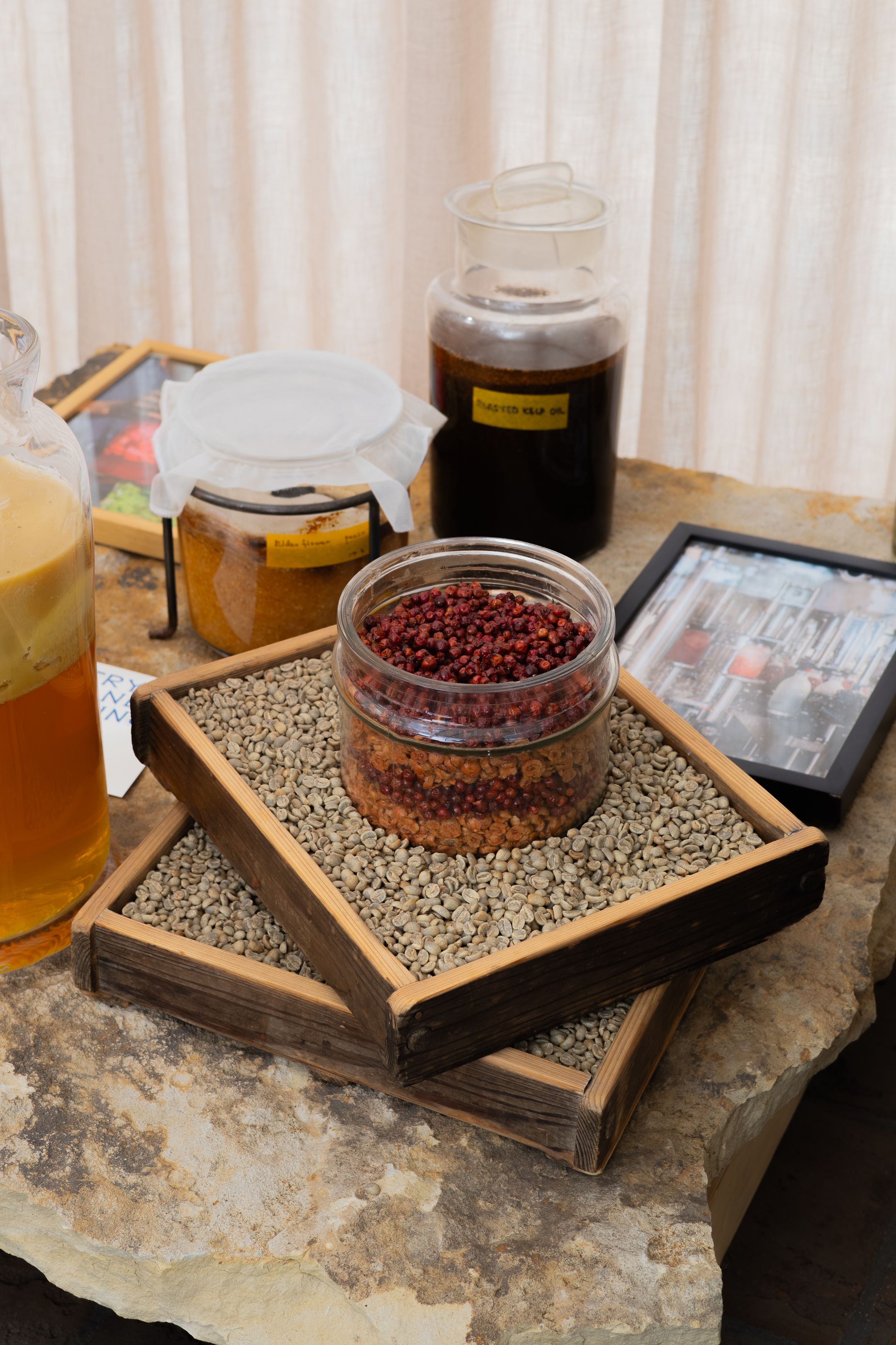 Dried green coffee beans displayed on wooden serving trays with various jars of processed coffee samples.