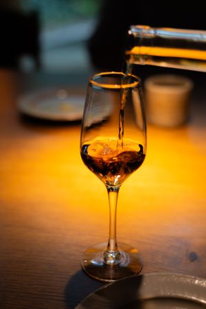 Wine glass with amber colored liquid glowing in warm lighting against dark background.