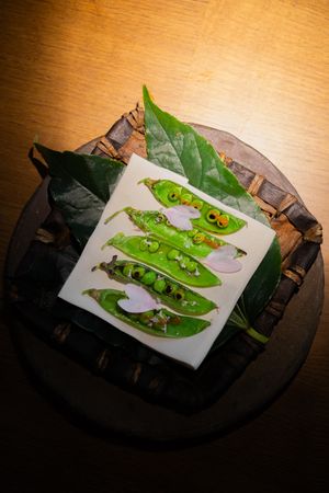 Fresh green pea pods artfully plated on white paper against dark wooden surface.