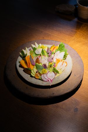 Beautifully plated salad with colorful vegetables and edible flowers on a rustic ceramic dish.