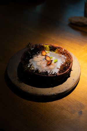 Artistic plating of seafood on a dark ceramic dish with dramatic lighting.