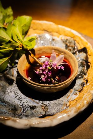 Purple edible flowers floating in dark liquid served in a rustic ceramic bowl.