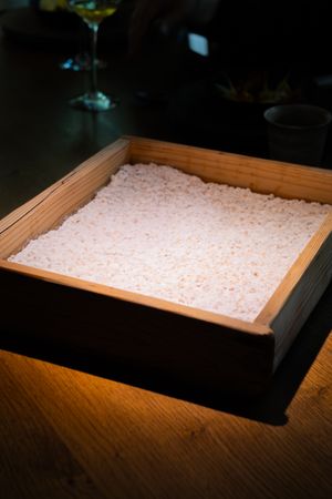A sequence of photos showing rice being spread out flat in a wooden box under illuminated lighting from above.