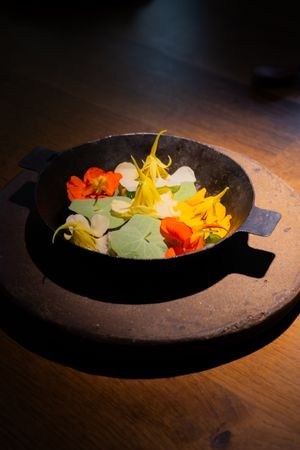 Colorful edible flowers arranged on a rustic dark plate against wooden surface.