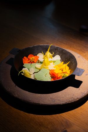 A minimalist plating of fresh edible flowers and microgreens on a dark ceramic dish under dramatic lighting.