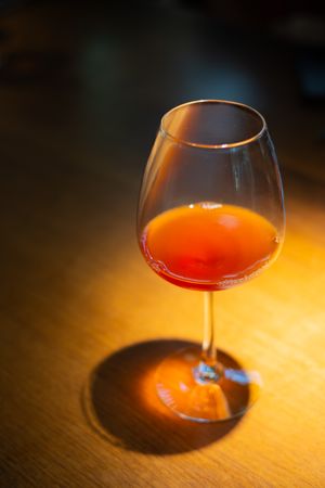 Close-up of a cognac glass with red liquid creating dramatic shadows on wooden surface in warm lighting.