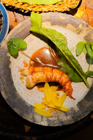 Sequence of shrimp appetizers artfully plated on stone dishes with yellow sauce and green garnish.