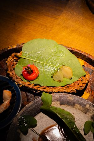 Artistic plating featuring green leaves and red garnish on a textured surface.