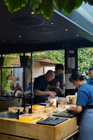 Chefs working at wooden prep stations in a modern restaurant kitchen with natural lighting.