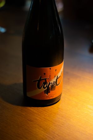 Wine bottle with orange label displayed on wooden surface under dramatic lighting.