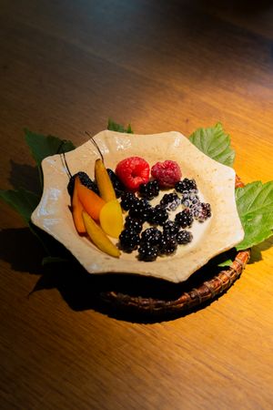 Fresh berries and fruit arranged on an artisanal ceramic plate with decorative leaves.