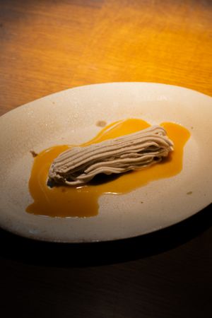 Brown noodles artistically arranged on a white plate with orange sauce.