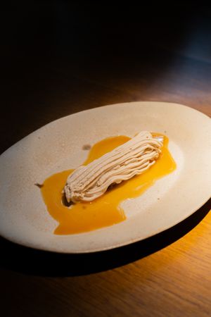 Creamy noodles elegantly plated on white dish with golden sauce under warm lighting.