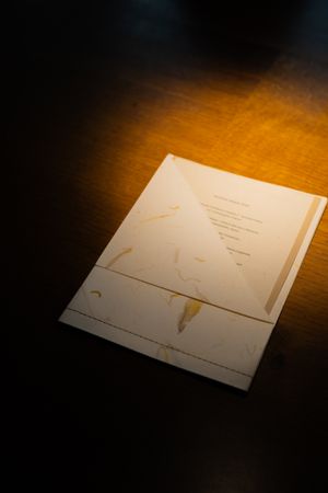 A minimalist white menu card or document illuminated by warm spotlight on a dark surface.