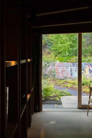 Interior view through large windows showing graffiti wall and green foliage outside.
