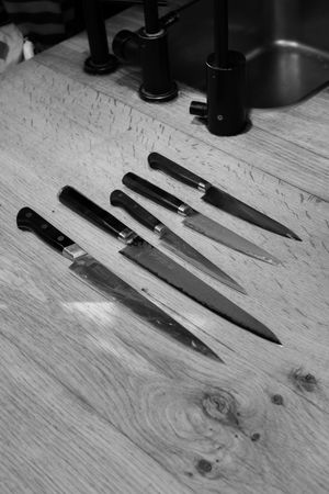 Collection of knives on a light wooden surface showing different blade styles and sizes.