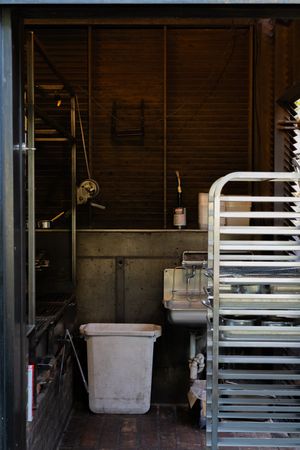Industrial kitchen storage area with white baking racks and storage bin against a wooden wall.