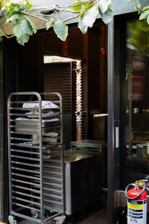 Outdoor seating area under green vine-covered pergola with industrial storage racks visible.