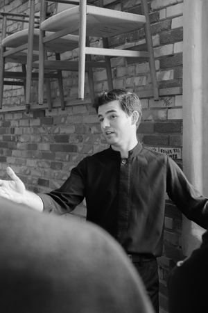 Black and white image showing repetitive poses of a person in dark clothing moving against a brick wall with metal poles.