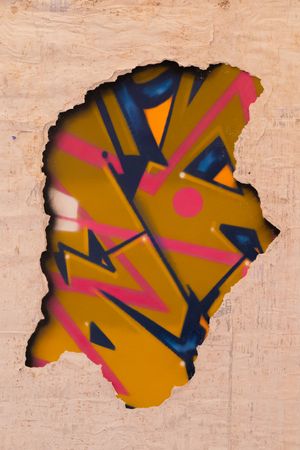 Abstract graffiti art with pink and blue angular shapes on a mustard yellow background showing through a textured beige frame.