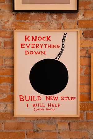 Series of framed art pieces on brick wall with text about knocking down and building new things.