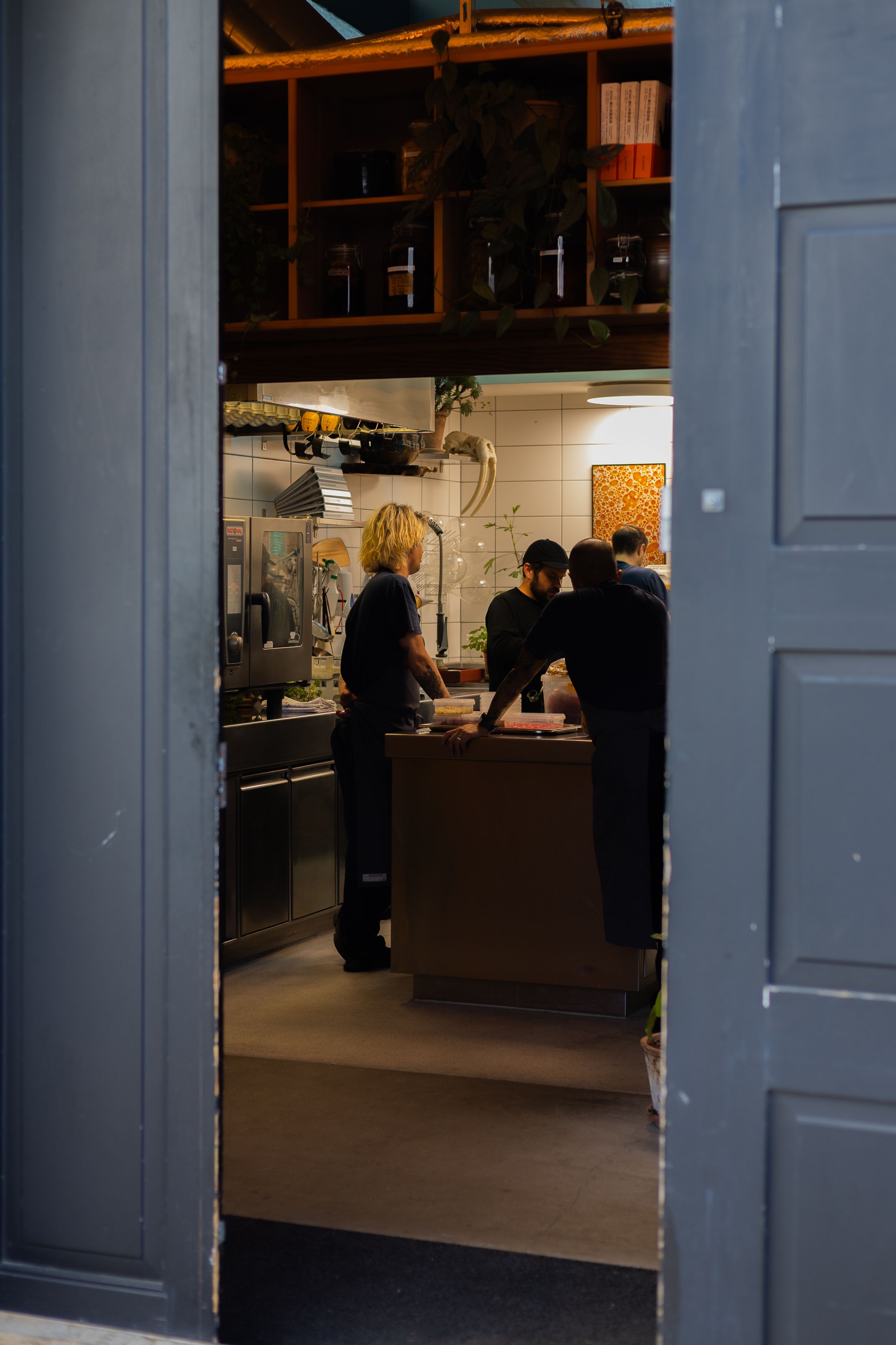 Interior view of restaurant kitchen through blue doorframe with staff working inside.