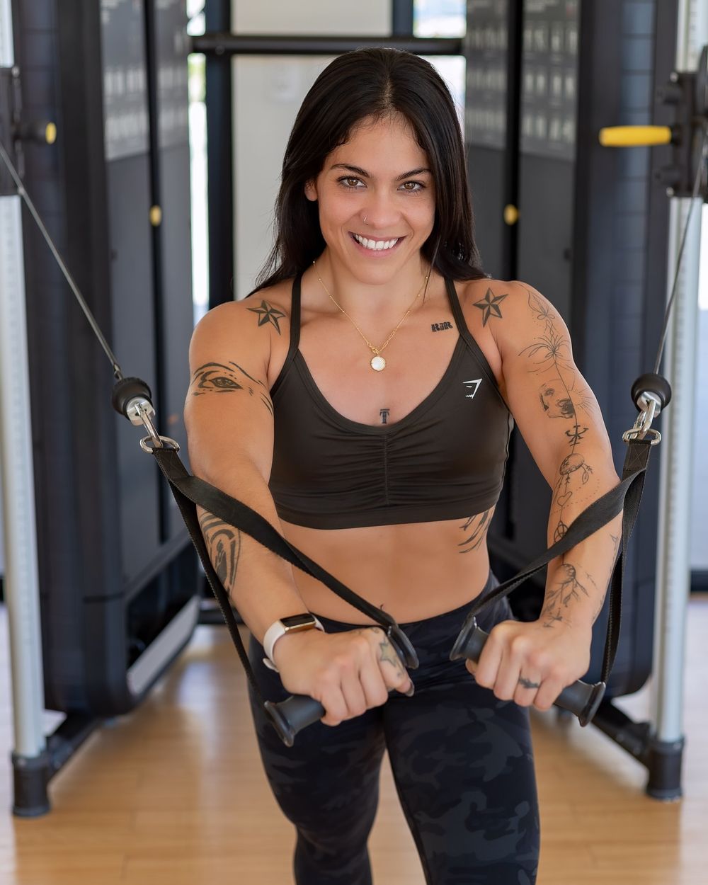 A person in workout attire demonstrates a cable machine exercise at a fitness center.