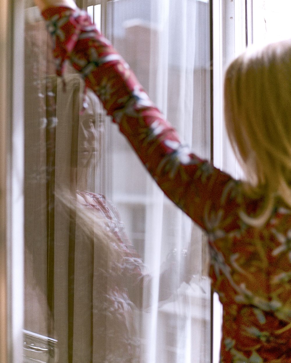 Person cleaning a window with a cloth in front of bright daylight, creating a reflective surface effect.