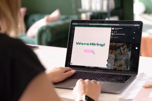 Someone working on a laptop displaying a webpage with pink text in a bright indoor setting.
