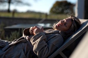 Relaxed person lounging in a reclining chair outdoors at sunset wearing a gray jacket.