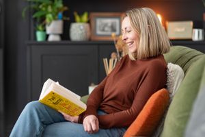 Someone relaxes in a cozy armchair while reading a book, surrounded by house plants and warm lighting.