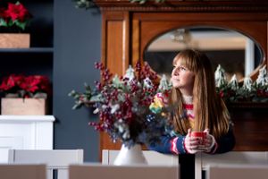Person sits by floral arrangement in vase with red and blue flowers against blue wall in cozy interior setting.