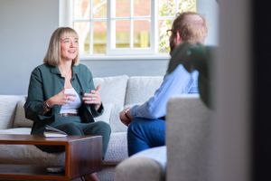 Two people having an animated conversation while sitting on a couch in a bright living room.
