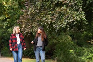 Two friends enjoying a casual walk in a park wearing plaid shirts and jeans on an autumn day.