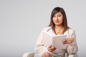 A business professional in a white sweater sits comfortably while holding and reading from an open book.
