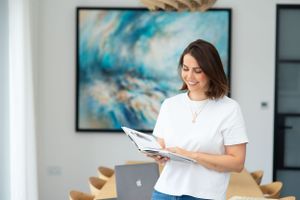 Professional woman in white t-shirt reviewing documents while standing in modern office with abstract art on wall.