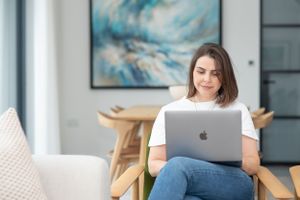 Person working from home on MacBook laptop while sitting comfortably in modern living room.