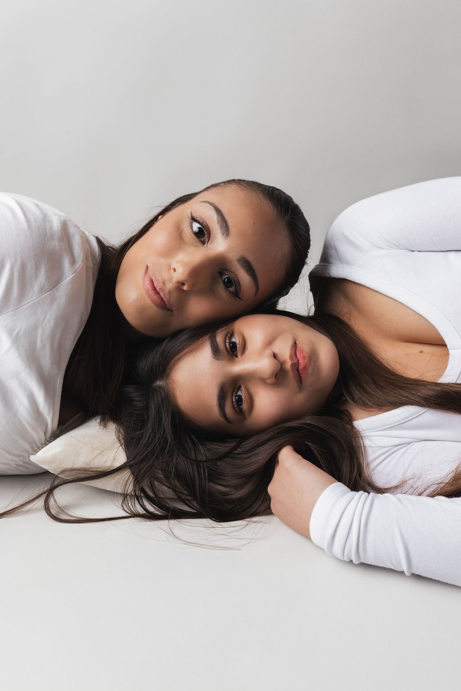Two people wearing white shirts lying close together against a neutral gray backdrop.
