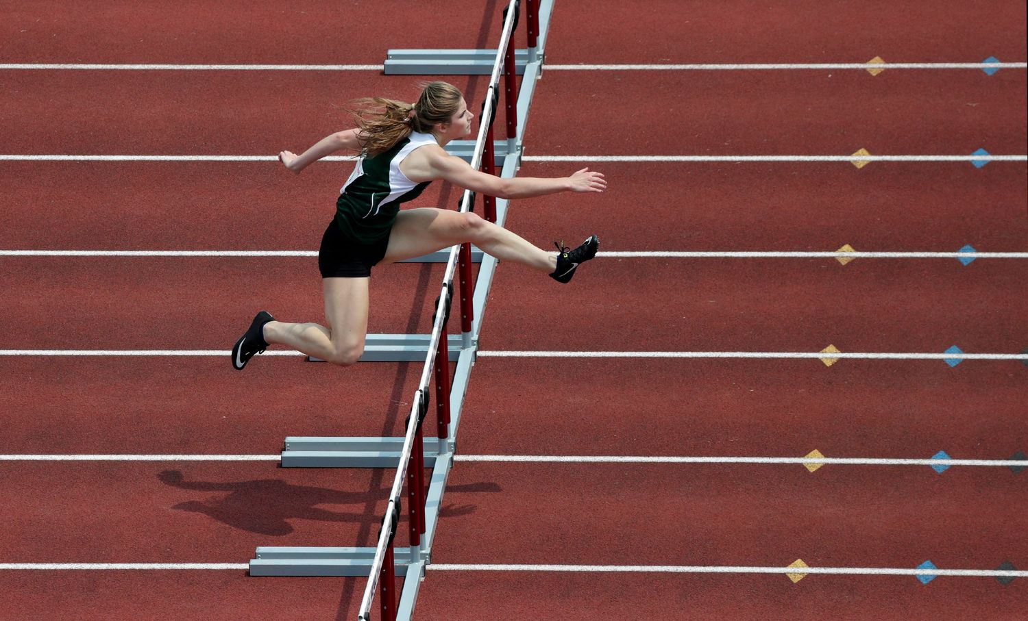 A hurdler leaps over a series of hurdles as seen from above.
