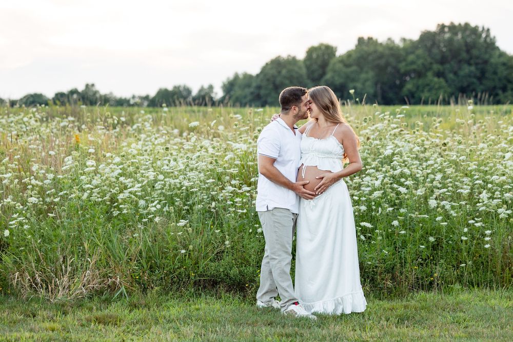 Couple sharing a tender moment in a field of white wildflowers during a maternity photo shoot outdoors.