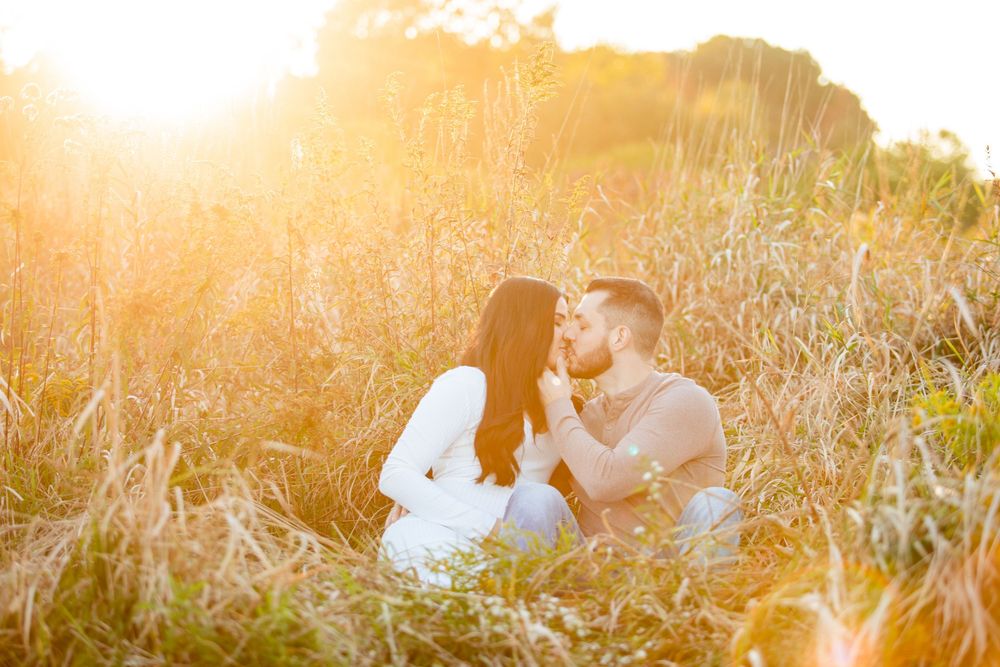 Couple sitting in golden field sharing a romantic moment during sunset with warm glowing light surrounding them.