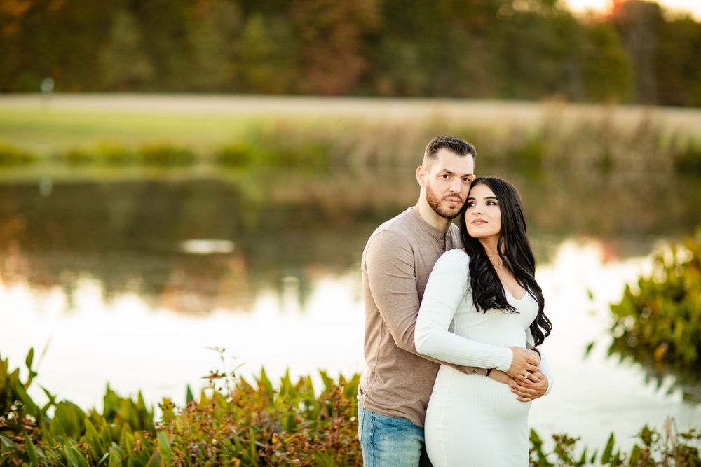 Couple embracing romantically by a serene lake at golden hour in an autumn park setting.