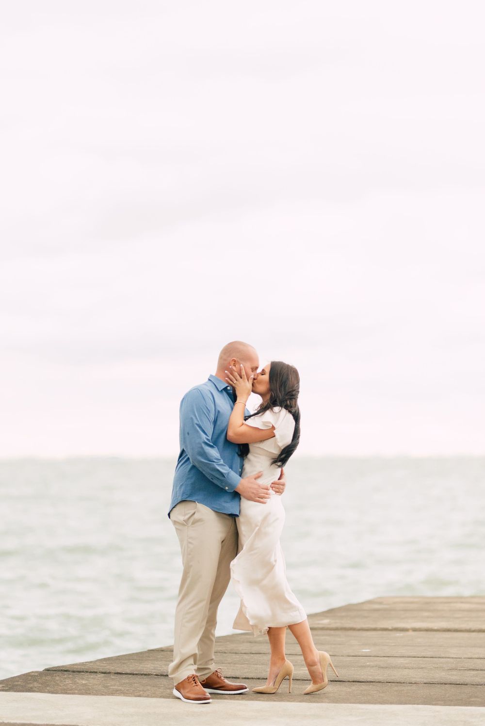 A romantic couple sharing a tender moment on a wooden pier by the ocean.