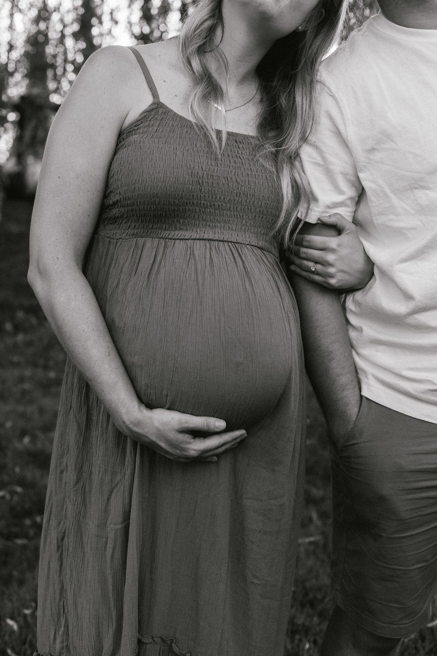 Black and white photo of a flowing maternity dress and gentle hands cradling a pregnant belly.