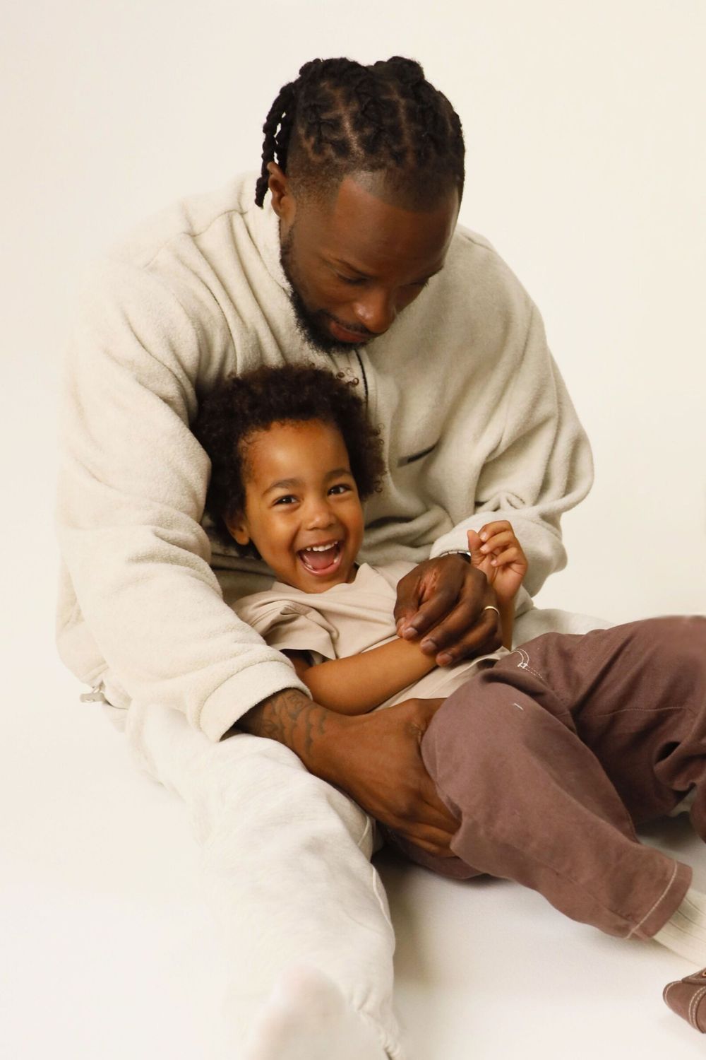 A playful tickling moment captured in white studio setting showing joyful laughter and connection.